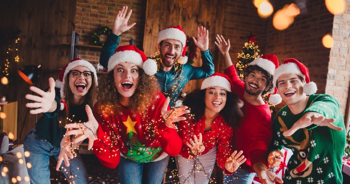 Grupo de amigos posando para foto, sorrindo com gorro de Natal em uma casa com decoração natalina.