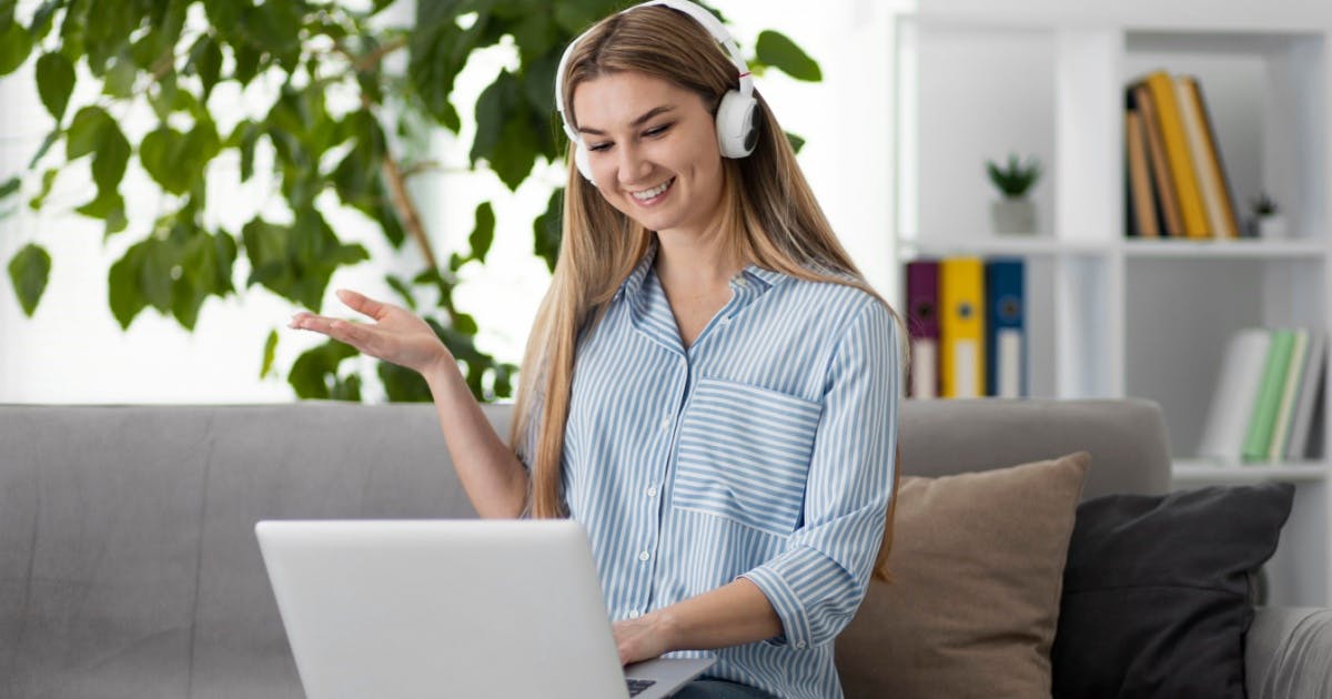 Mulher com fones de ouvido sentada no sofá, usando um laptop para aprender inglês.