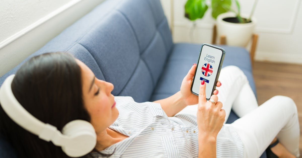 Mulher usando um smartphone com a bandeira britânica na tela, para aprender inglês.