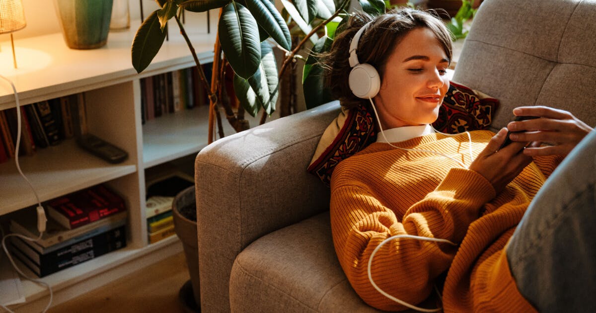 Uma mulher sentada no sofá usando fones de ouvido, imersa em sua música ou podcast.