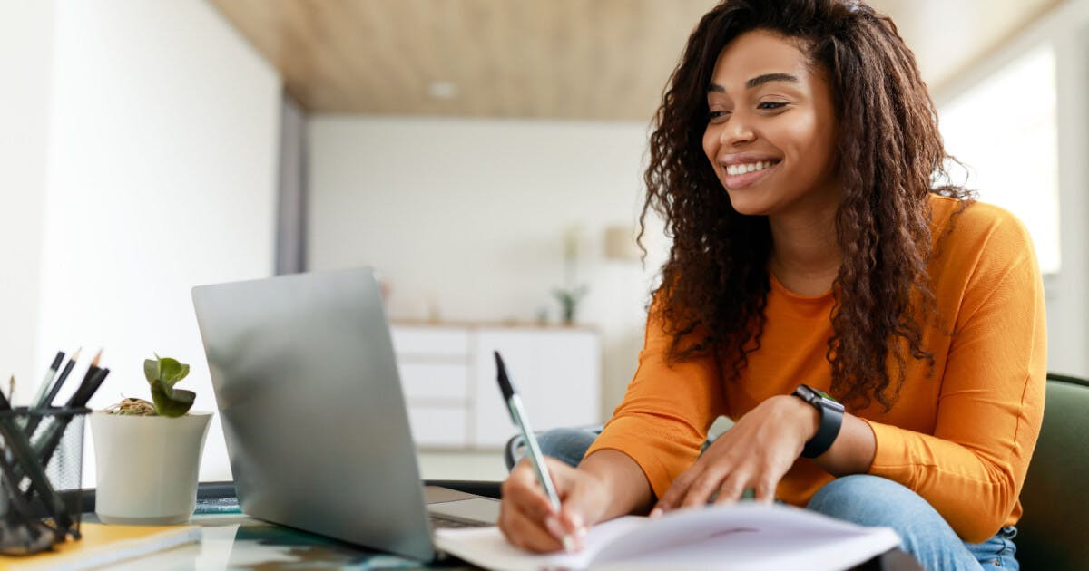 Uma mulher sorridente senta-se à mesa com um laptop, transmitindo uma sensação de alegria e produtividade.