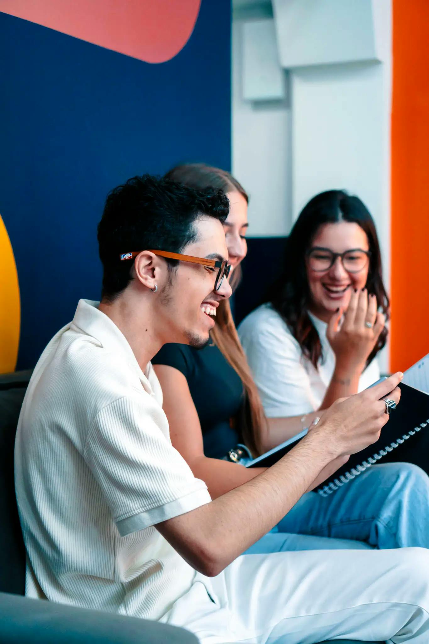 Três jovens sorrindo enquanto revisam materiais didáticos da Phenom Idiomas, sentados em um ambiente colorido e descontraído.