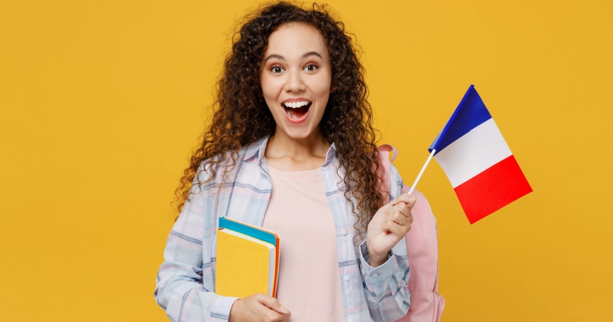 Garota sorrindo segurando uma bandeira da frança e o material de sua aula de francês.