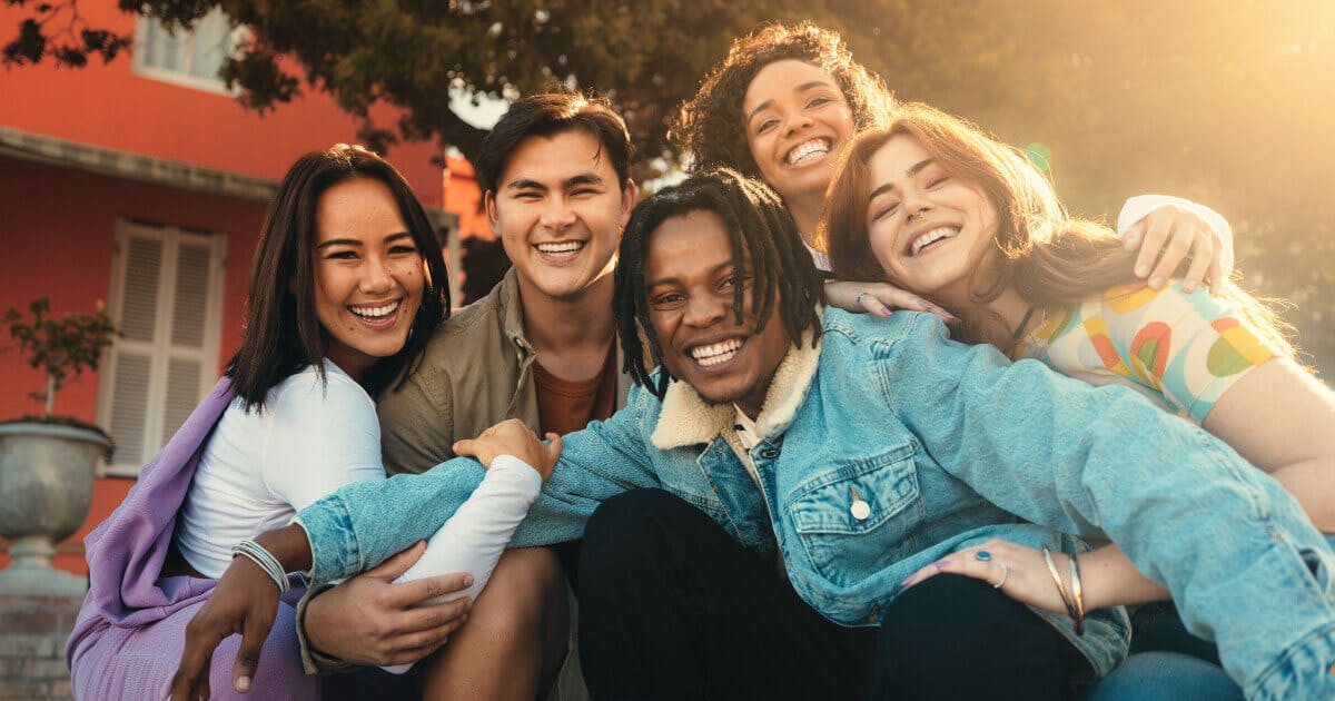 Um grupo de jovens posando para uma foto, sorrindo e demonstrando alegria em um ambiente descontraído.