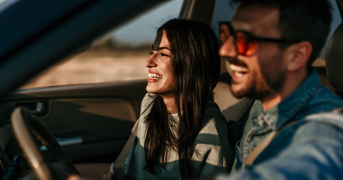 Homem de óculos e mulher dentro de um carro sorrindo.