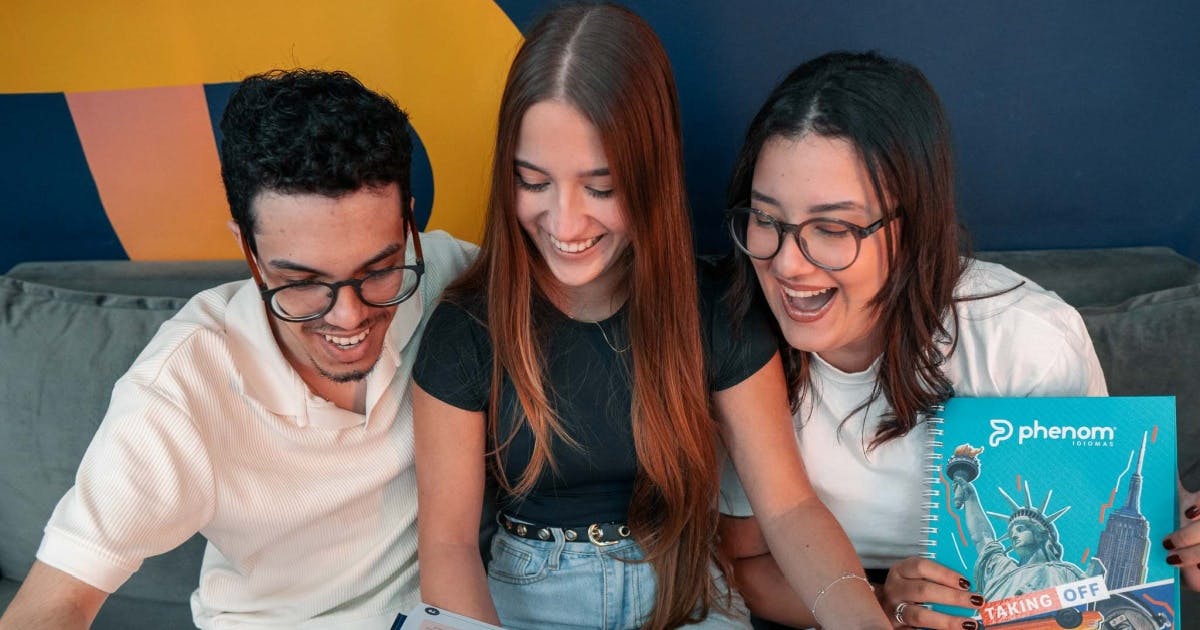 Três estudantes (duas mulheres e um homem) sorrindo e com os livros da Phenom Idiomas.