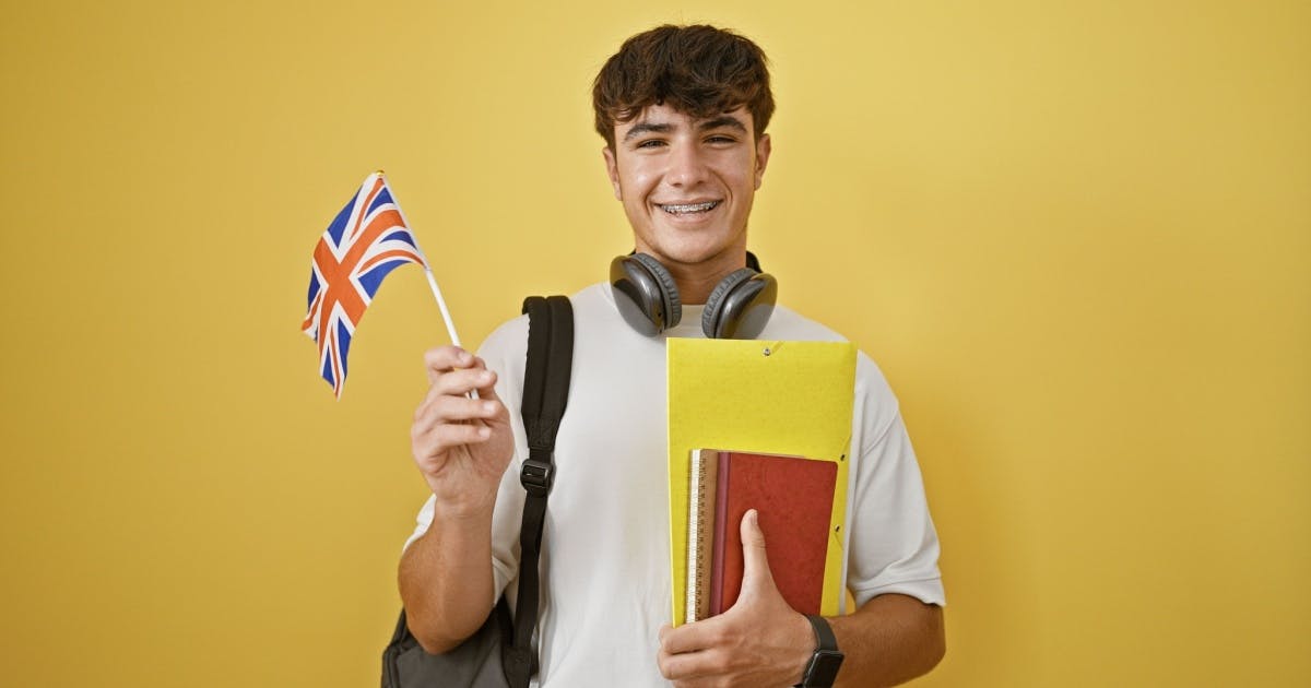 Estudante com livros e uma bandeira da Grã-Bretanha, com fones de ouvido no pescoço, para estudar ouvindo músicas em inglês.