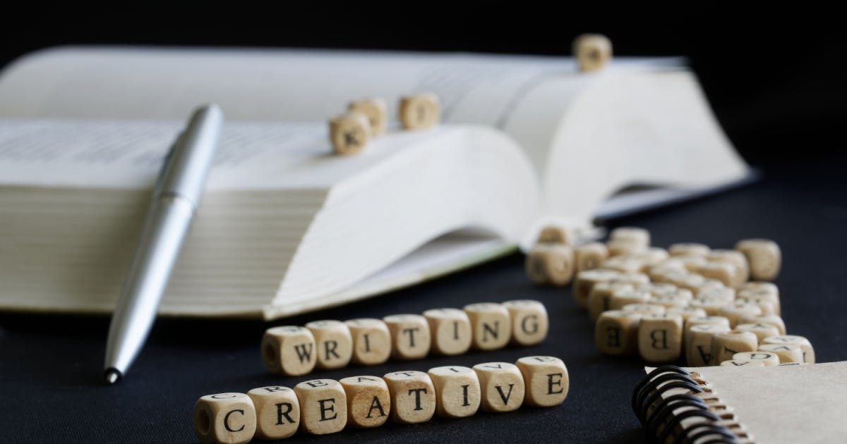 Livro sobre escrever em inglês aberto com vários pequenos cubos de madeira e alguns deles formando a frase "Writing creative"