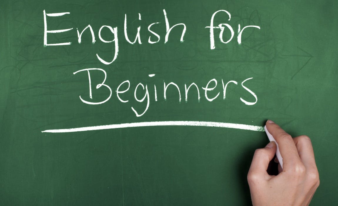 Uma mão segurando um giz branco, traçando uma linha em baixo da frase "English fo Beginners".