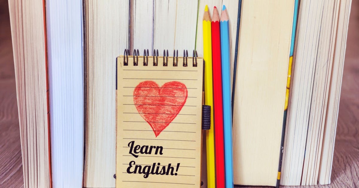 Caderno com um coração  desenhado acima da frase "Learn English", encostado em alguns livros em inglês para iniciantes.