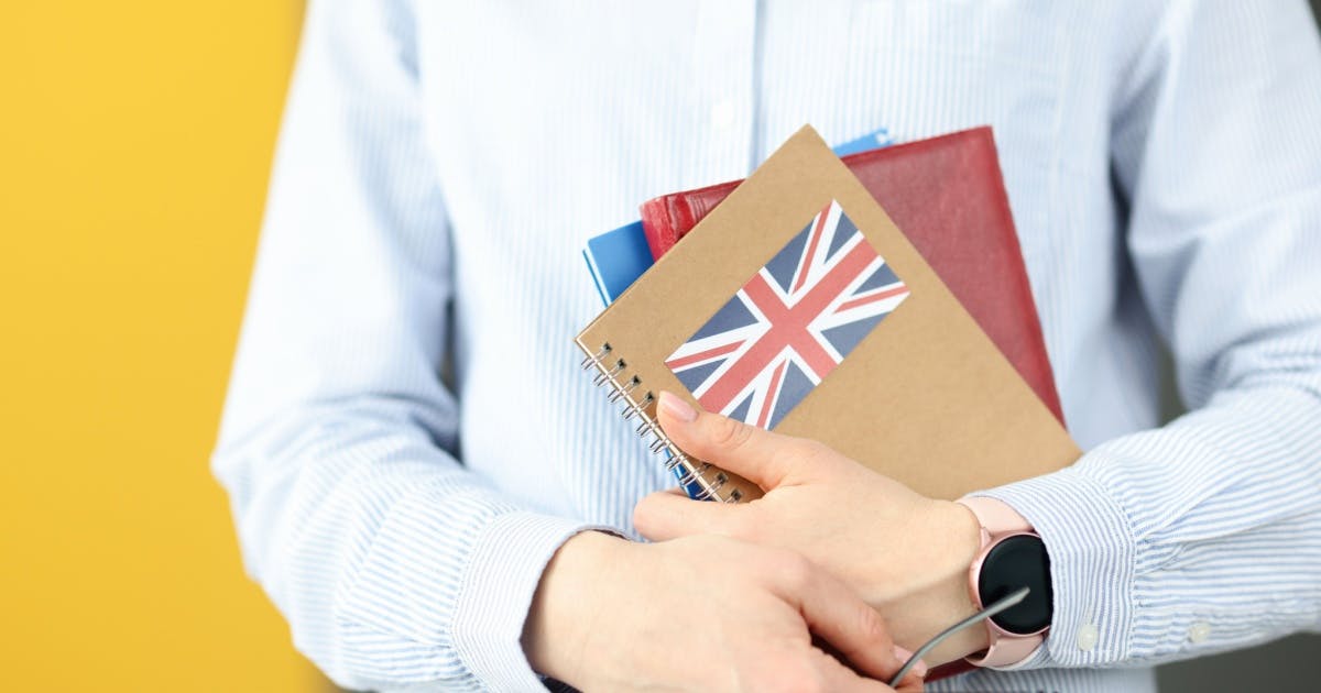 Homem segurando três livros de curso de inglês para viagem, com o da frente tendo a bandeira da Grã-Bretanha na capa.