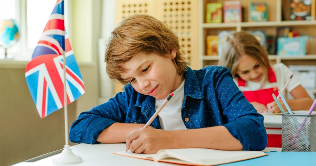 Menina escrevendo texto em inglês iniciante com um lápis em um caderno, com uma bandeira da Grã-Bretanha ao lado.