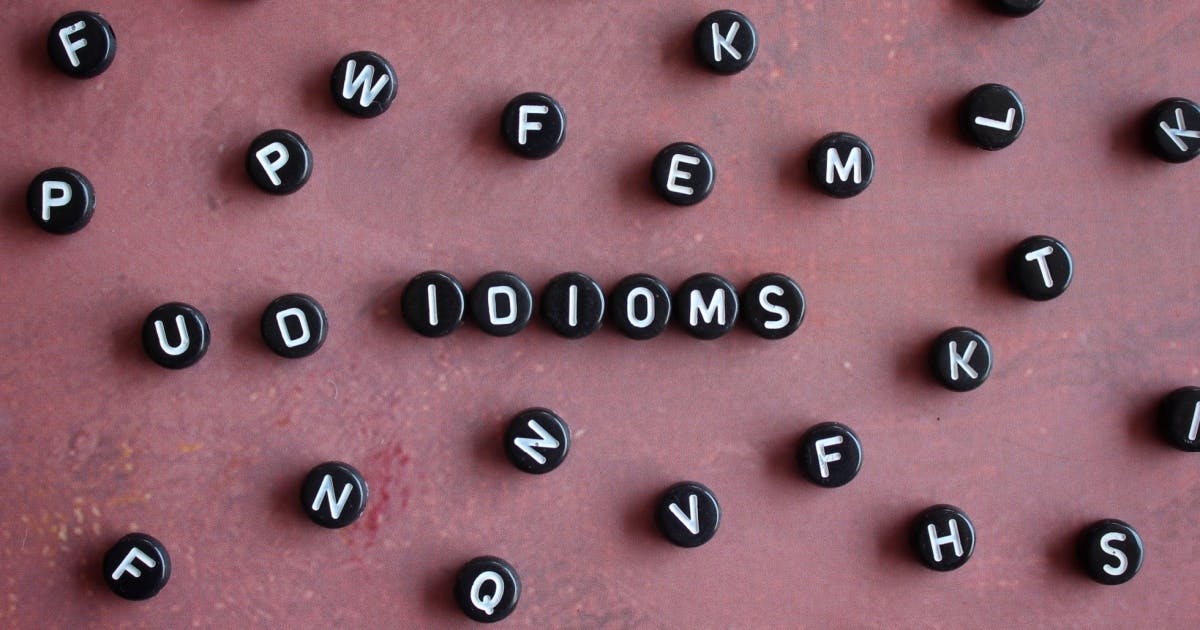 Algumas peças de plástico pretas com letras em branco, espalhadas, com as peça no centro da tela formando a palavra "idioms".