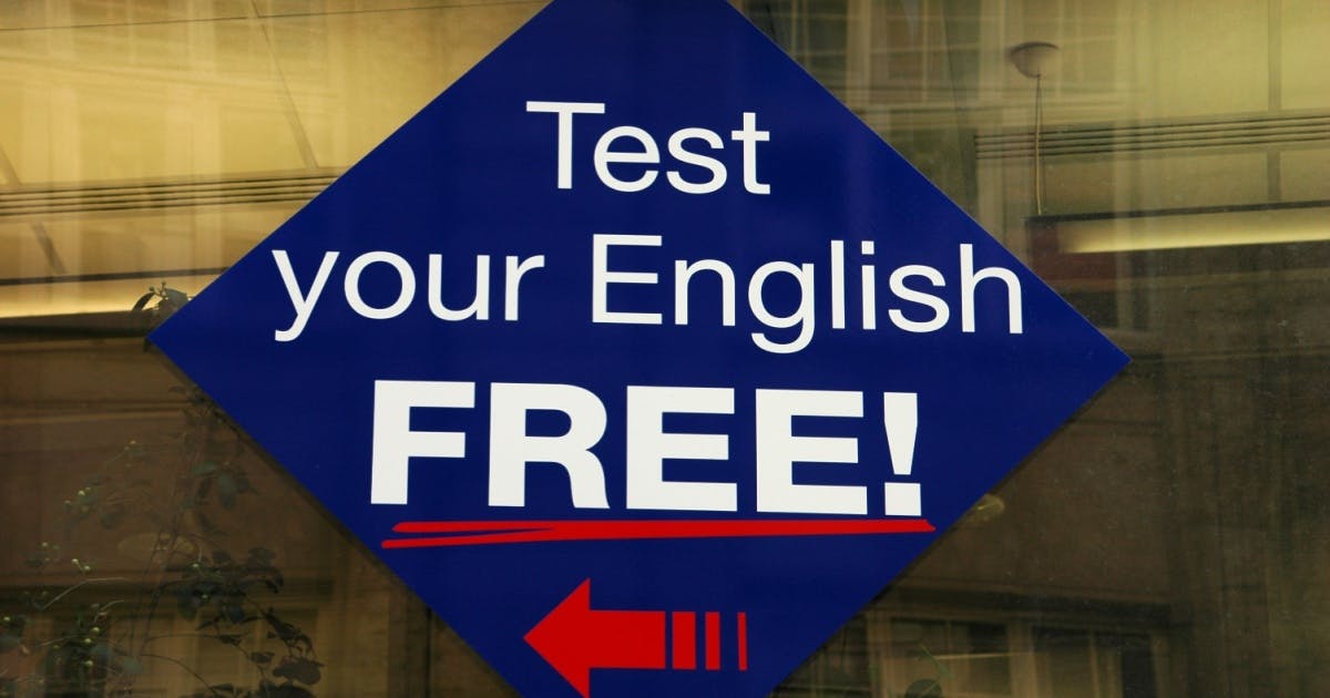 Adesivo azul colado em um vidro com a frase "Test your English FREE!", convidando as pessoas para fazerem um teste de nível de inglês.