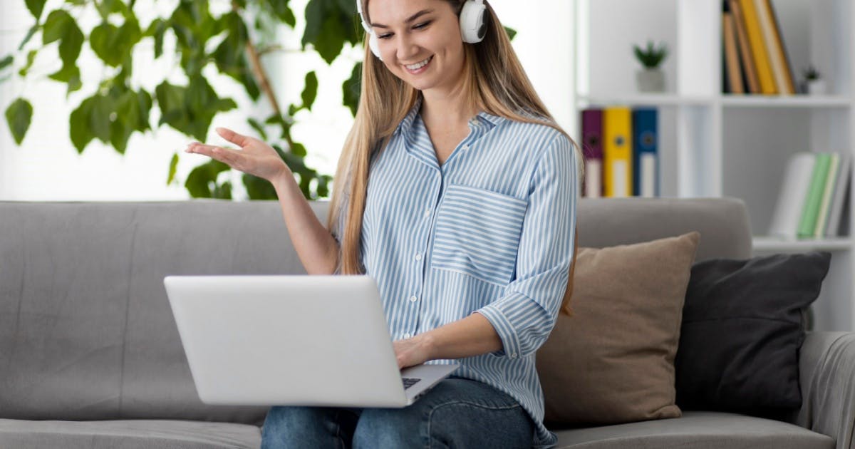 Mulher sentada, sorrindo usando um fone de ouvido, com um notebook aberto no colo, tentando descobrir como aprender inglês.