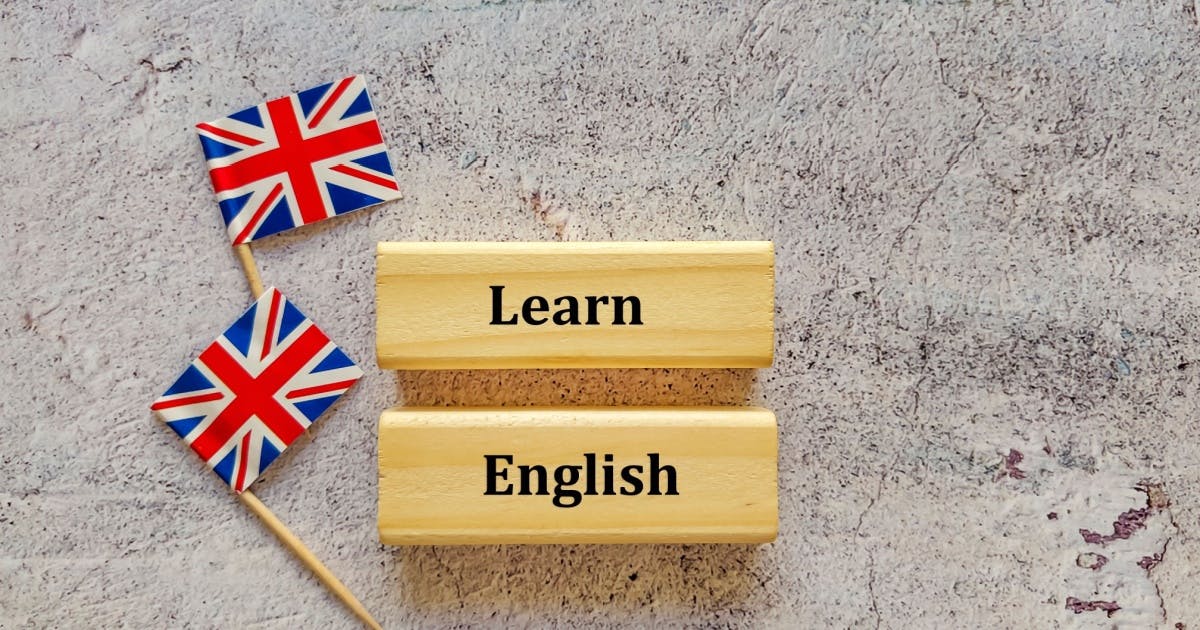 Duas peças de madeira formando a frase "Learning English", ao lado de duas bandeiras da Grã-Bretanha.