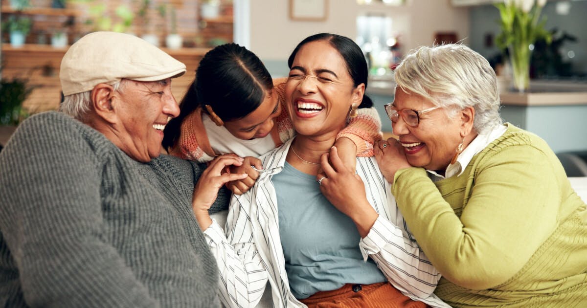 Uma família de quatro pessoas sorrindo e rindo juntas em um momento de alegria e união.