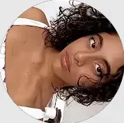 Mulher em close com cabelo cacheado e expressão facial natural em foto circular, com fundo claro e tom de pele bem iluminado.