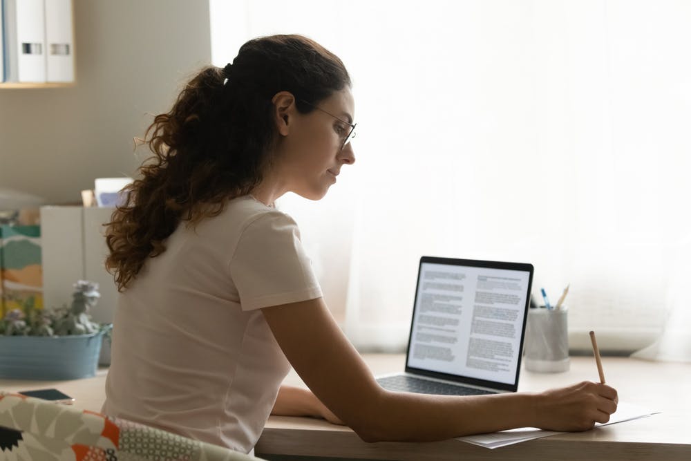 Mulher sentada em uma mesa usando um laptop para ler textos em inglês.