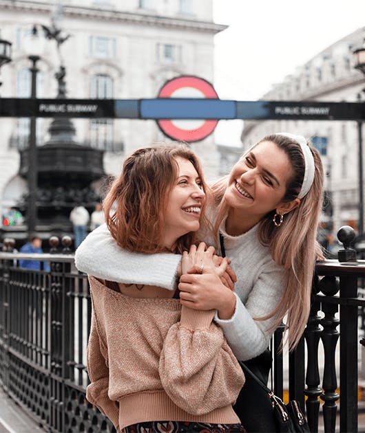 Duas amigas se abraçando em frente do metrô de Londres