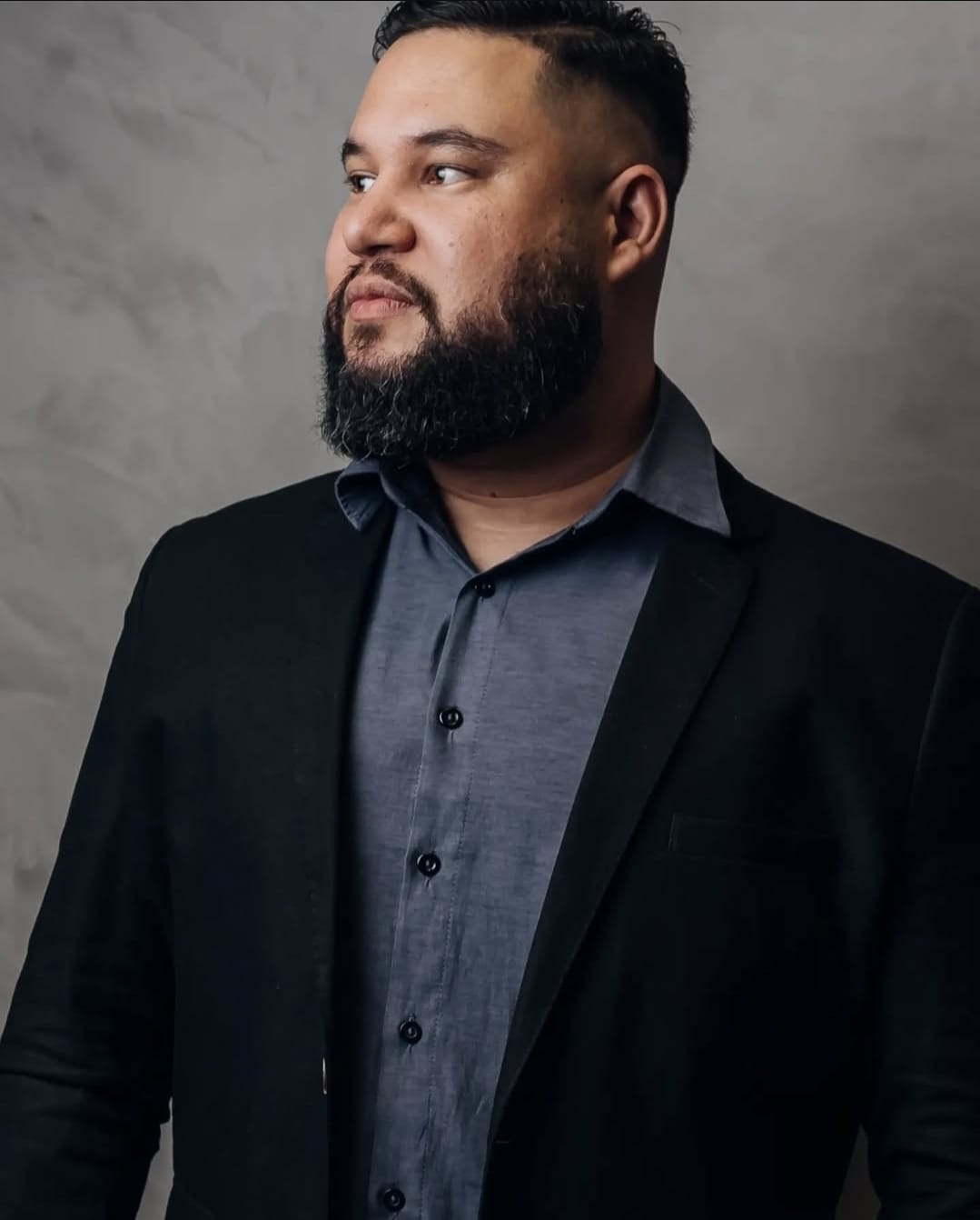 Homem de pé de blazer e com uma camisa cinza.