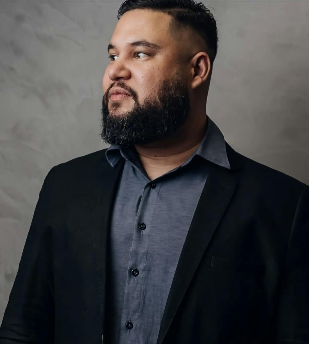 Homem de pé de blazer e com uma camisa cinza.