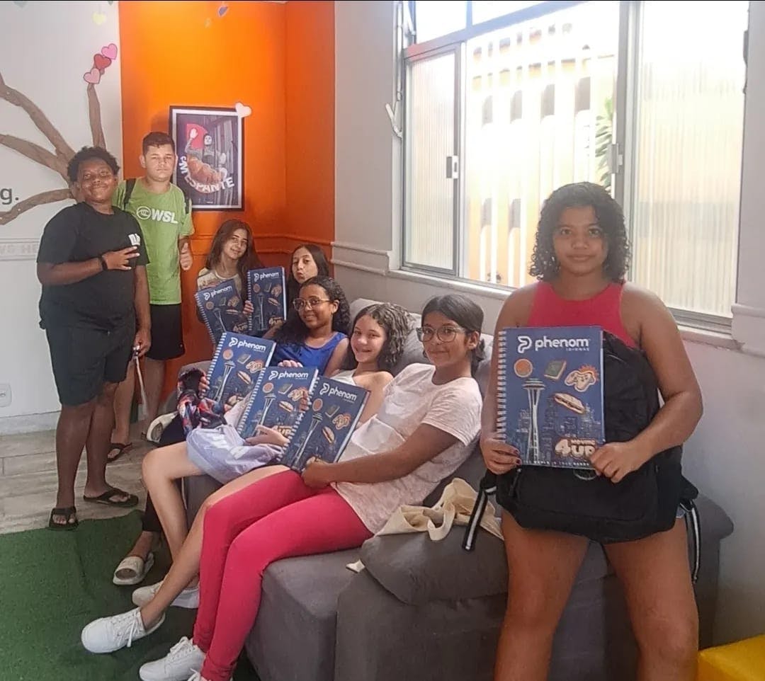 Grupo de alunos de uma unidade Phenom sentados em um sofá da escola, enquanto seguram seus livros.