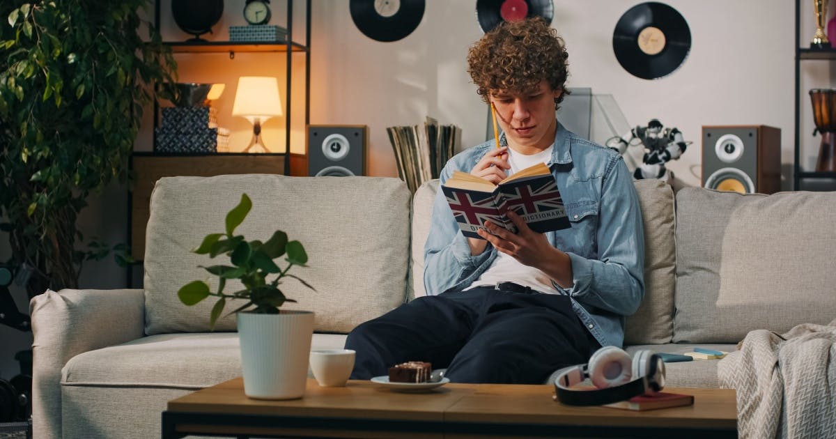 Um jovem sentado no sofá, lendo um livro de inglês com atenção para se tornar poliglota.