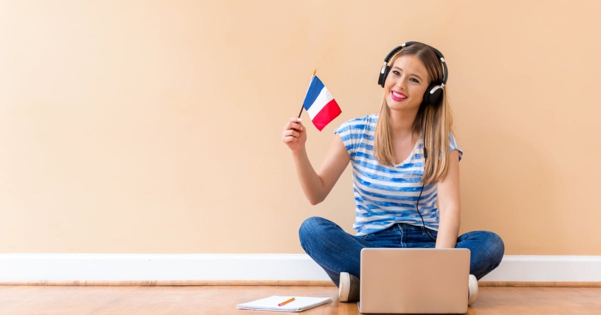 Menina sentada na frente do notebook, segurando uma bandeirinha da frança