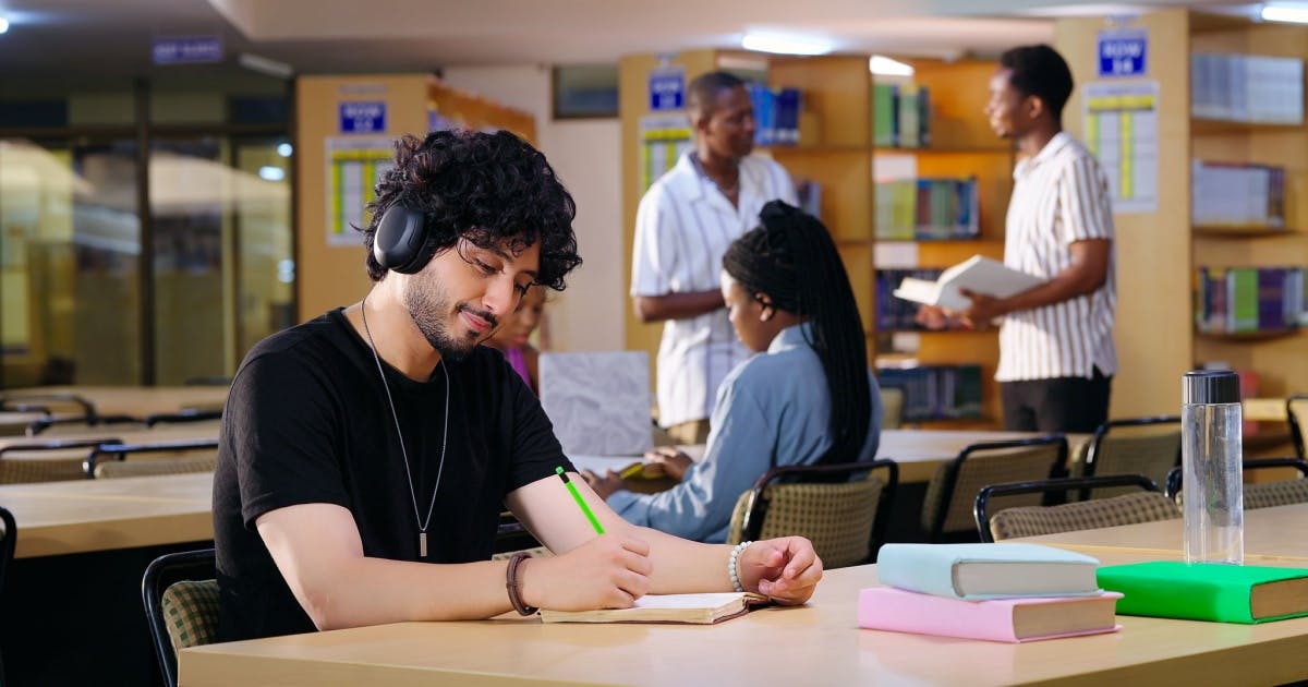 Homem jovem sentado em uma biblioteca estudando com uma música para estudar.