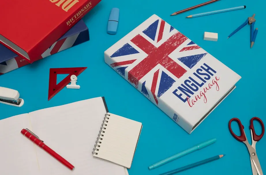 Matrial de estudo em mesa azul com livro “English language” mostrando a bandeira do Reino Unido, caderno com elástico, lápis, canetas, tesoura e itens de papelaria