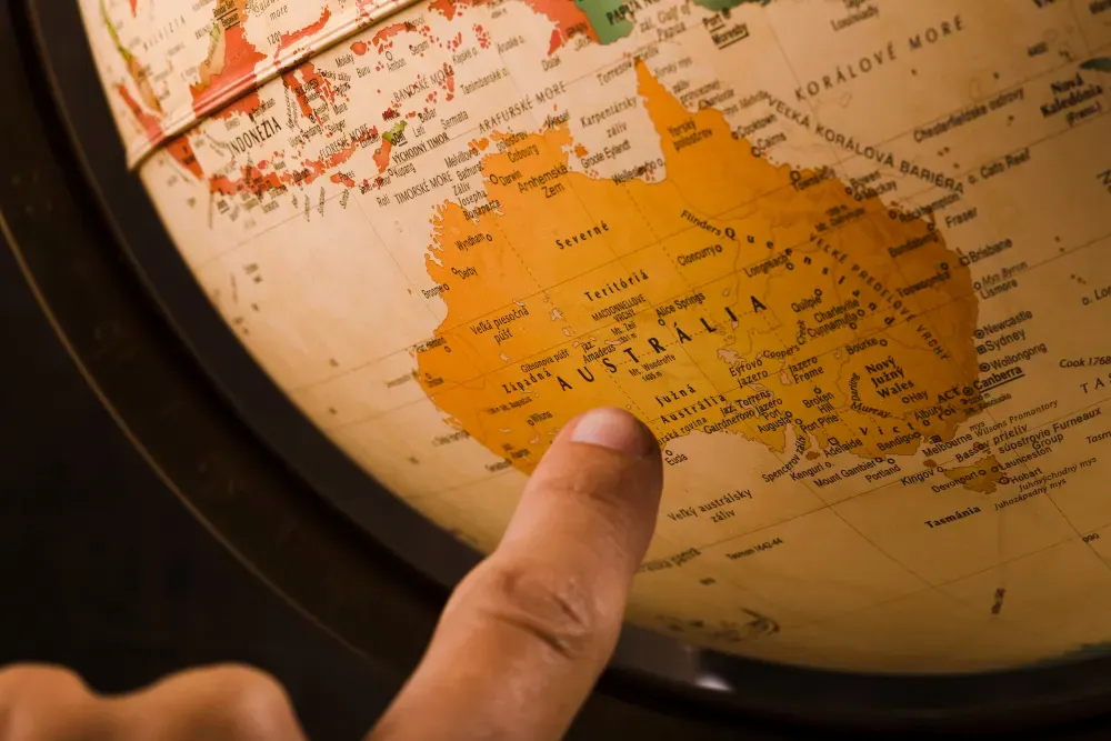 Detalhe de um globo terrestre com a mão apontando para a América do Norte, mostrando países e limites em mapa físico e político, em ambiente escuro.