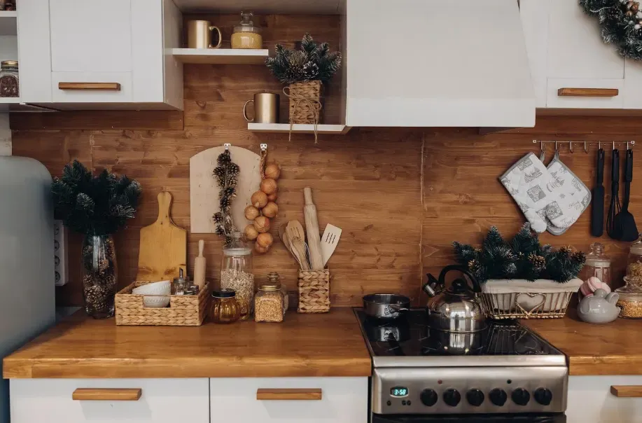 Cozinha rústica e aconchegante decorada para o Natal, com balcão de madeira, enfeites verdes, panelas e utensílios, além de temperos e potes sobre as bancadas.