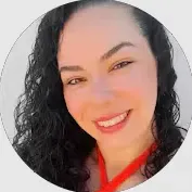 Retrato sorridente de uma mulher com cabelo cacheado escuro, brincos discretos e expressão gentil, em fundo claro e iluminação suave.