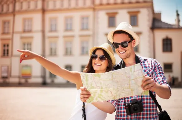 Casal de turistas em viagem, usando chapéus e óculos escuros, abrindo um mapa em uma rua de cidade europeia ao ar livre, sorrindo