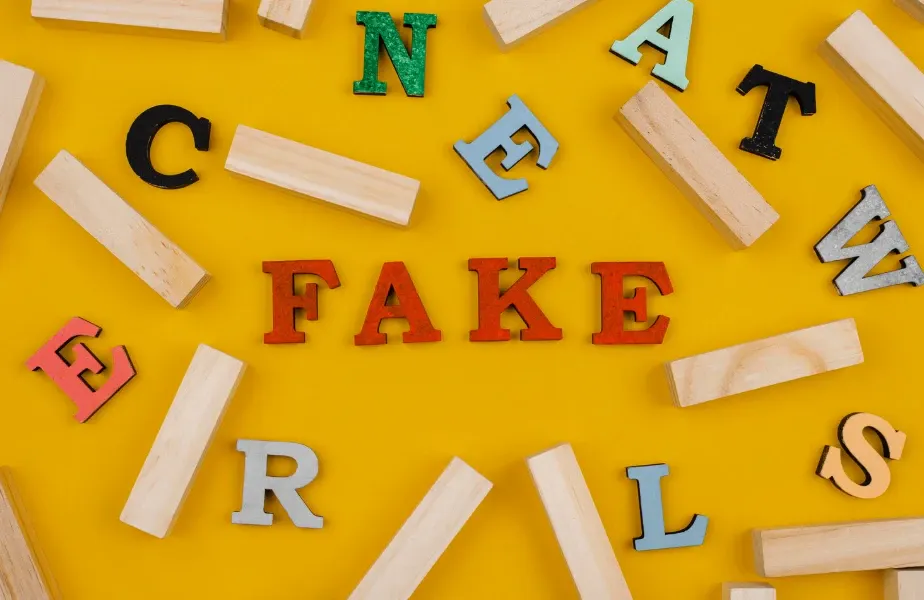 Imagem com letras de madeira coloridas formando as palavras “FAKE” e outras letras soltas, sobre fundo amarelo vibrante, em composição tipográfica para alerta sobre falsificações.