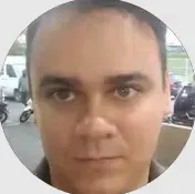 Retrato em close de um homem em ambiente urbano, com expressão séria, olhando diretamente para a câmera e enquadrado em formato circular.