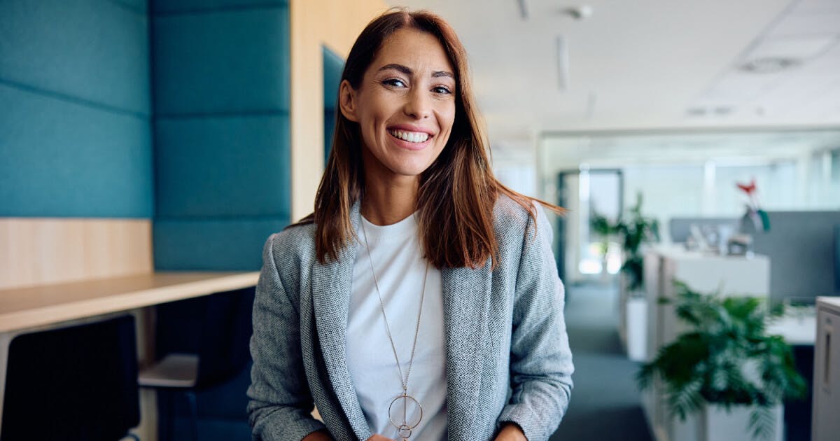 Uma mulher sorrindo em um escritório, transmitindo uma atmosfera de felicidade e profissionalismo.