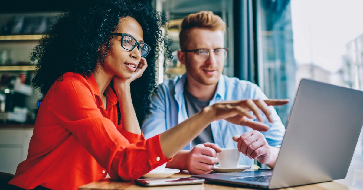 Um homem e uma mulher sentados à mesa com um laptop, discutindo ou trabalhando juntos em um ambiente colaborativo.