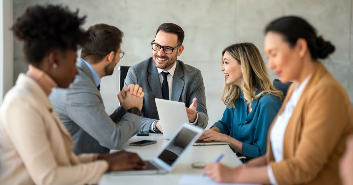 Homem e sua equipe sentados do trabalho diante de uma mesa com os notebooks abertos enquanto ele trabalha a gestão de pessoas