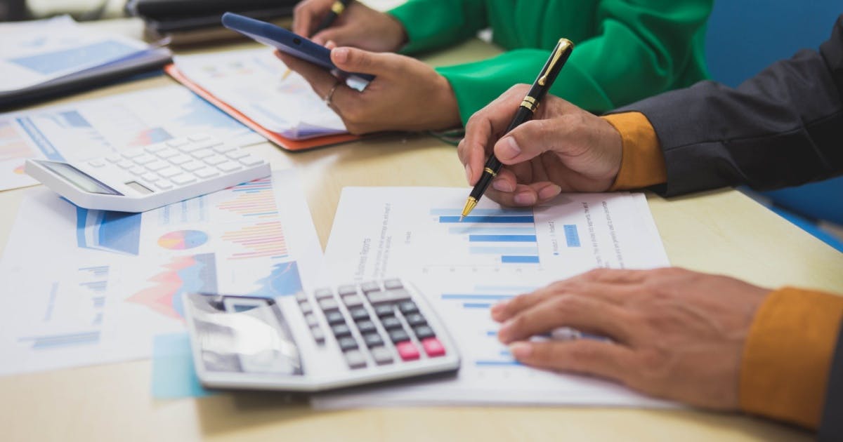 Homem mostrando como organizar as finanças da empresa em uma folha com gráficos ao lado de uma calculadora e em cima da mesa.