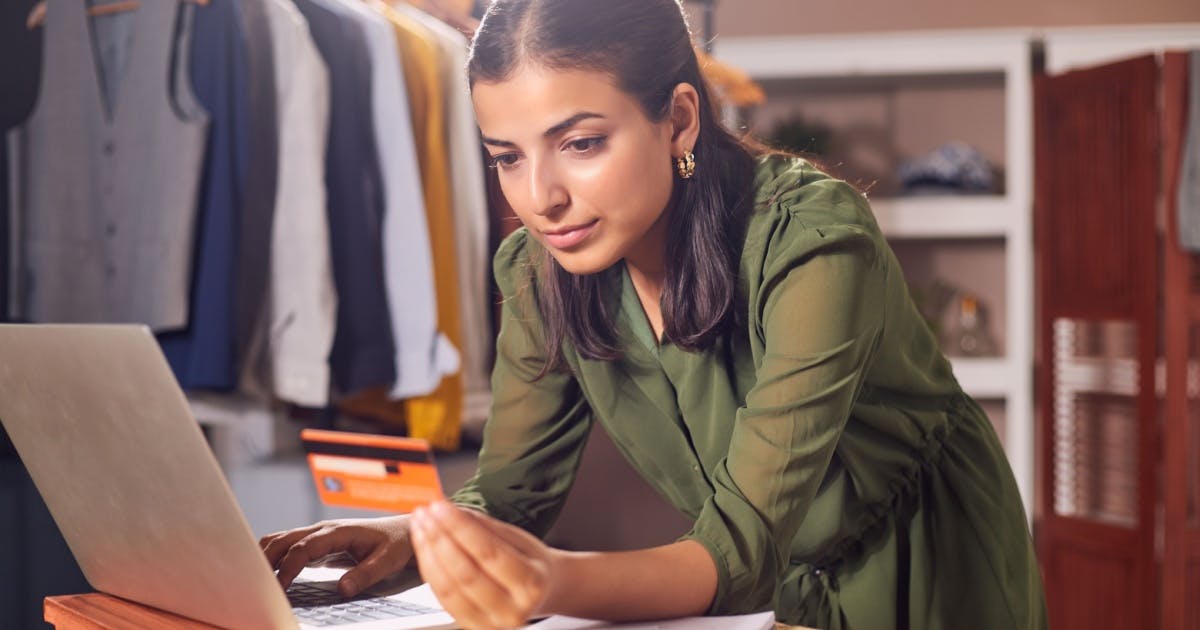 Mulher de camisa verde no trabalho em busca de sua independência financeira, consultando os dados de uma conta em um cartão.