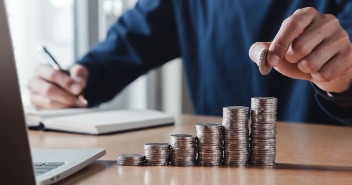 Homem em busca de independência financeira empilhando moedas em somas crescentes e anotando em um caderno.