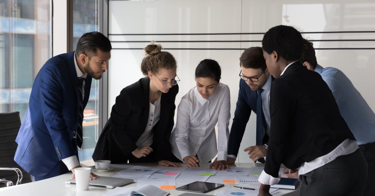 Equipe reunida em uma sala, analisando resultados de microfranquias em tornos de uma mesa com alguns papéis e objetos.