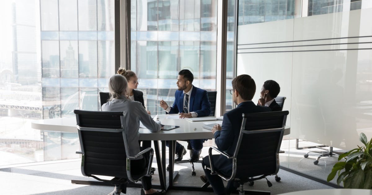 Equipe sentada reunida, conversando sobre os resultados de microfranquias em torno de uma mesa com alguns papéis e objetos.