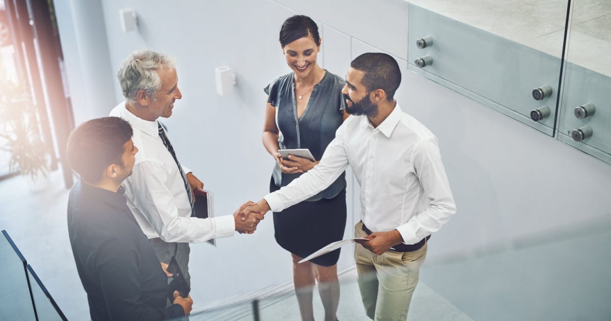 Grupo de pessoas de franquias em alta de pé, sorrindo e se cumprimentando em um ambiente corporativo.