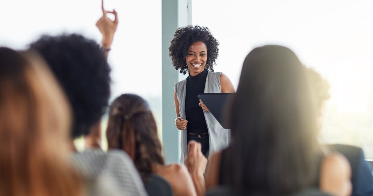 Mulher de pé falando sobre franquias em alta para um grupo de pessoas sentadas em algumas cadeiras em uma sala.