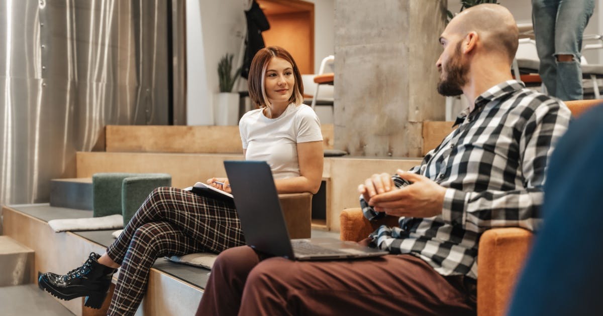 Um homem com um notebook aberto no colo e uma mulher sentados, conversando sobre como começar um negócio do zero.