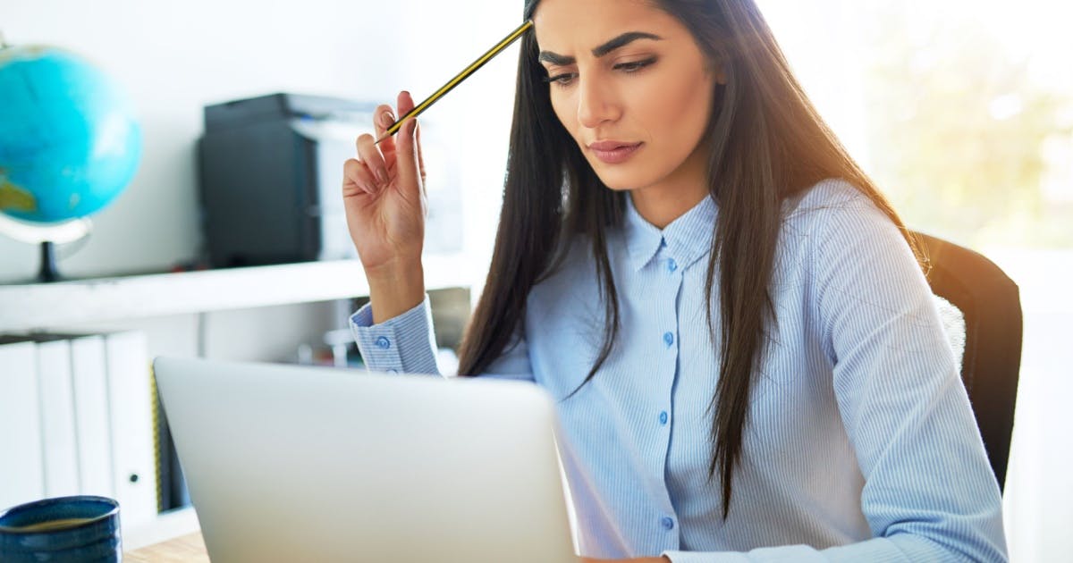 Mulher sentada com um notebook na frente dela, coçando a cabeça com um lápis, ao pensar em como começar um negócio do zero.