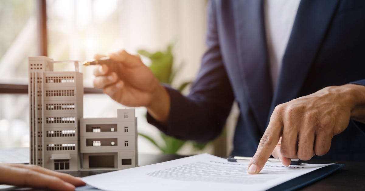 Homem em uma mesa de escritório, verificando cláusula em um contrato de franquia na frente de outra pessoa antes de assinar.